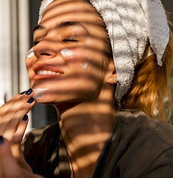 A woman applying lotion to her face.